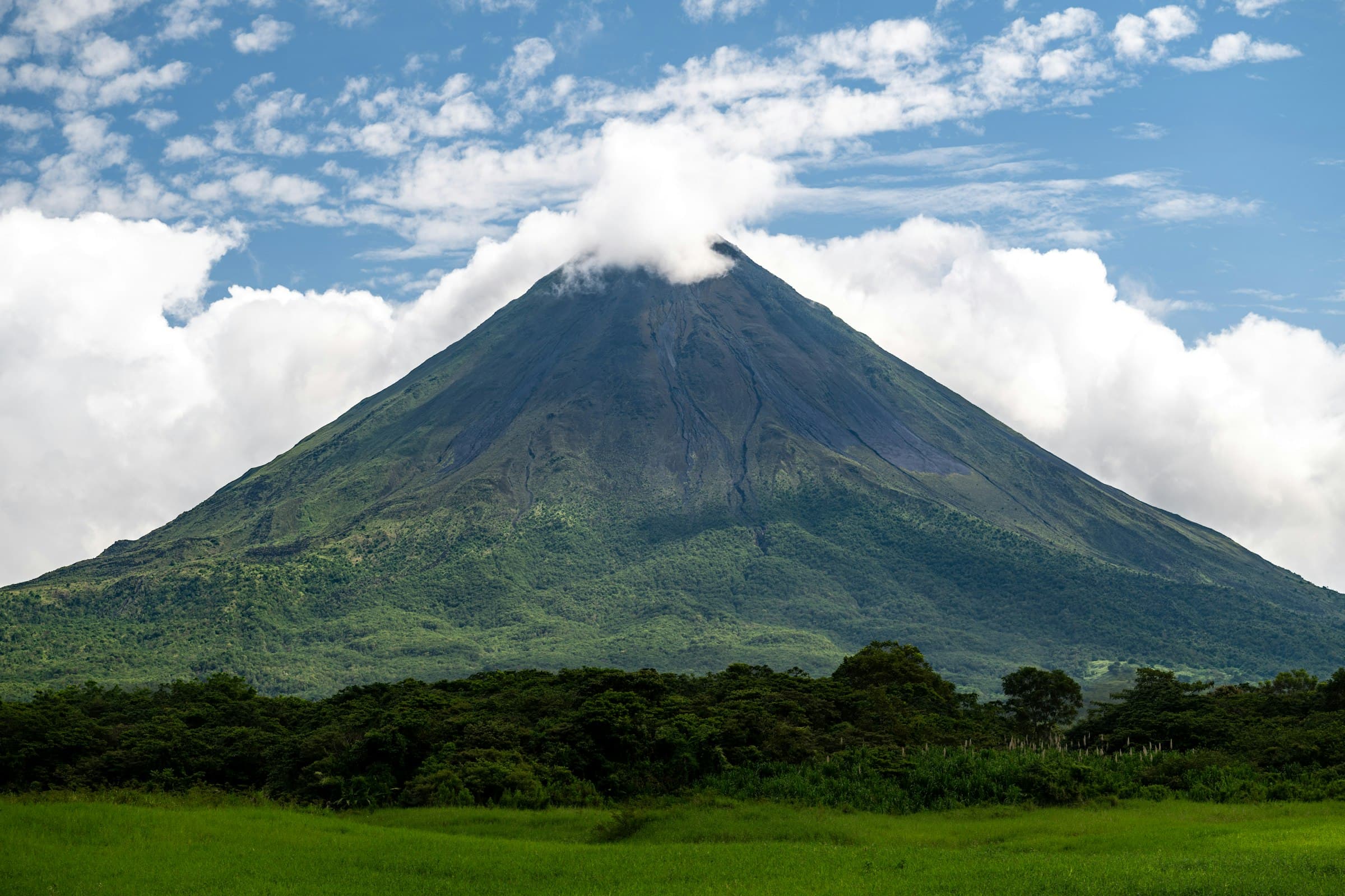 The cone of the Arenal Volcano seen from La Fortuna, its base covered in rainforest and clouds over the summit